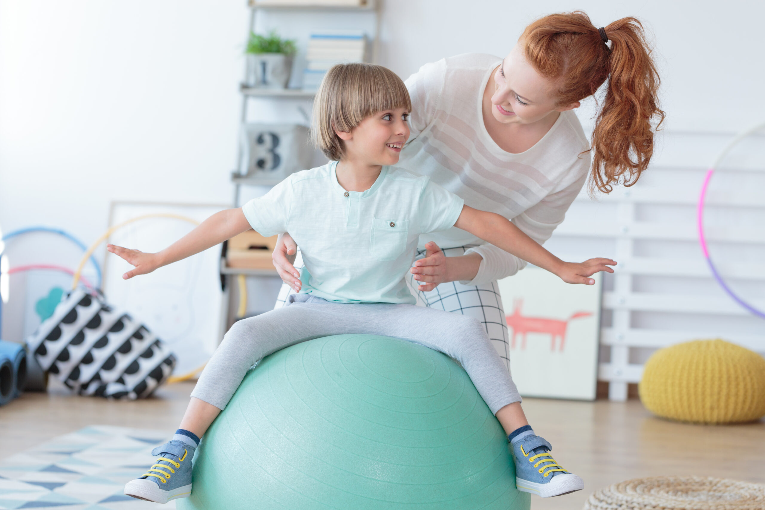 Physical,Therapist,Assisting,Little,Boy,Sitting,On,Gym,Ball,During Pediatric Physical Therapy