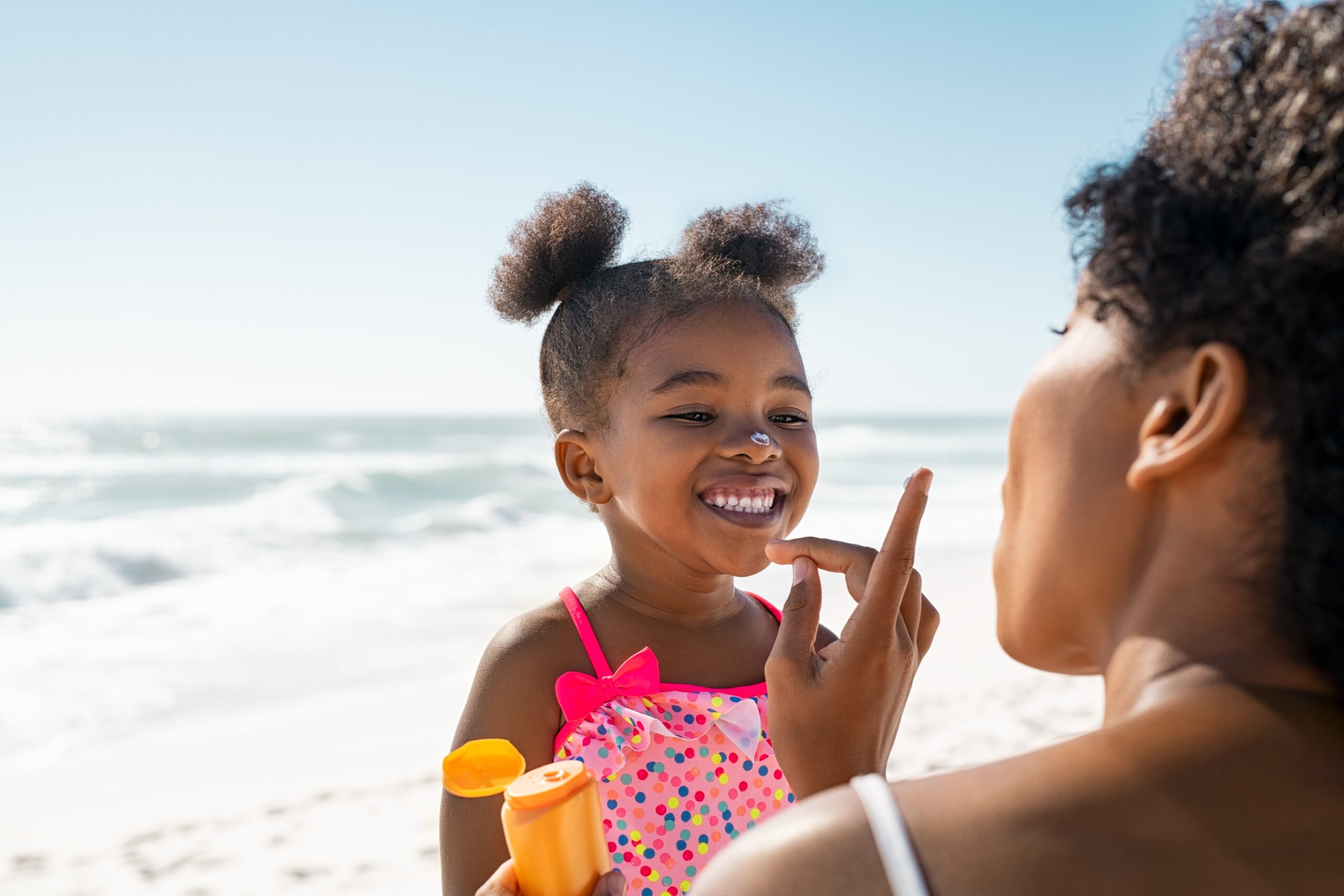 Young,Mother,Applying,Protective,Sunscreen,On,Daughter,Nose,At,Beach child using sunscreen- heat exhaustion vs heat stroke in children